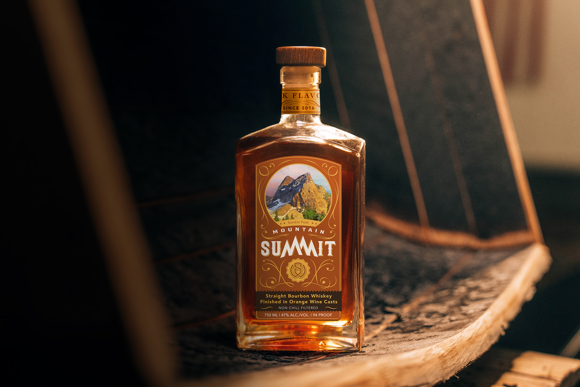Mountain Summit: Orange Wine Cast Finished Whiskey Bottle - Professionally photographed. Sitting atop an aging barrel with a glass next to it.